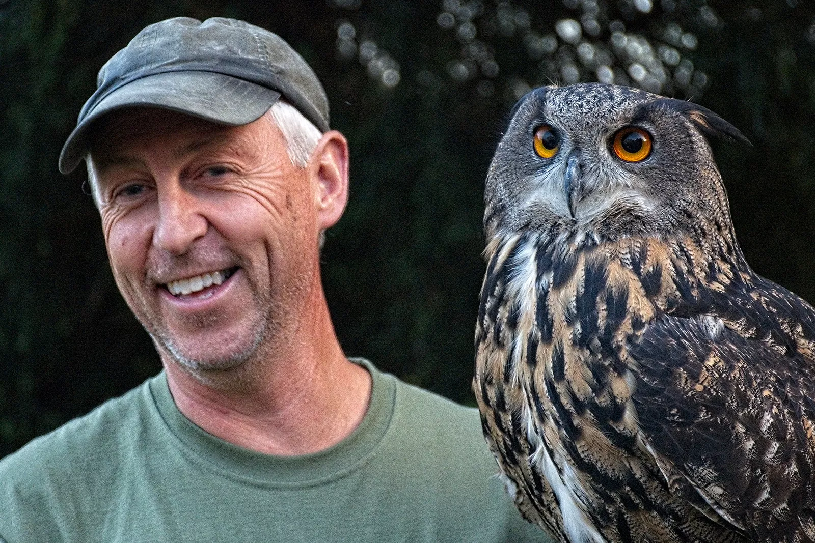 Man wearing a hat smiling next to an owl