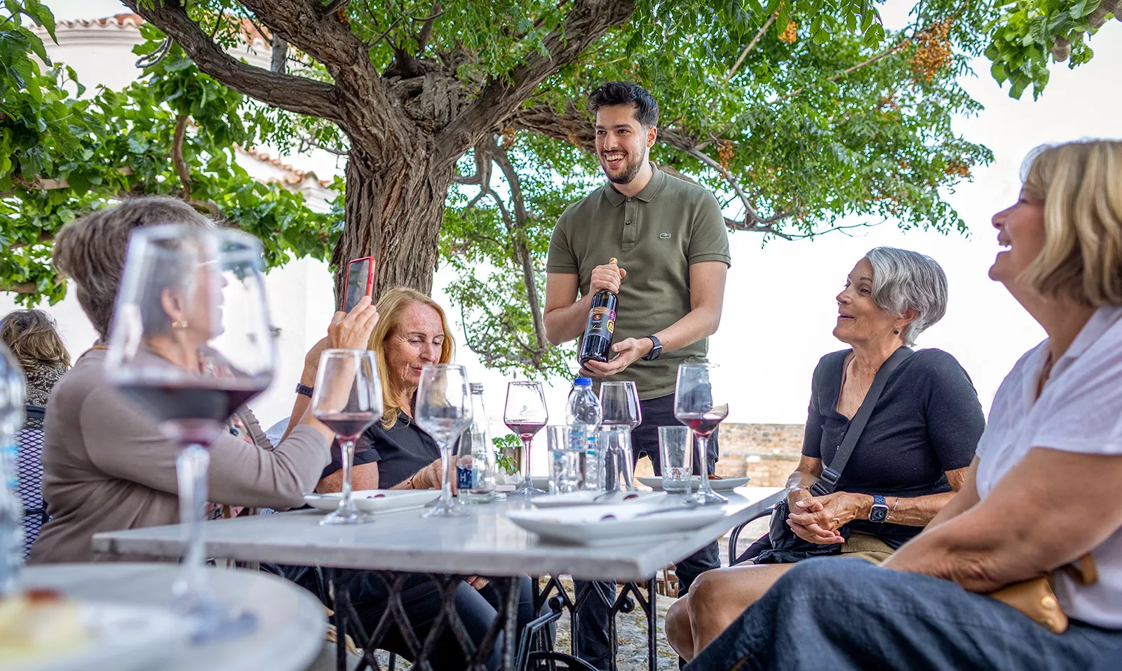 One man holding a wine bottle around four women siting down