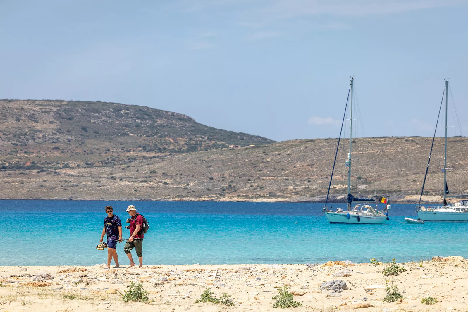 Two people on the beach walking next to the ocean with their shoes in hand