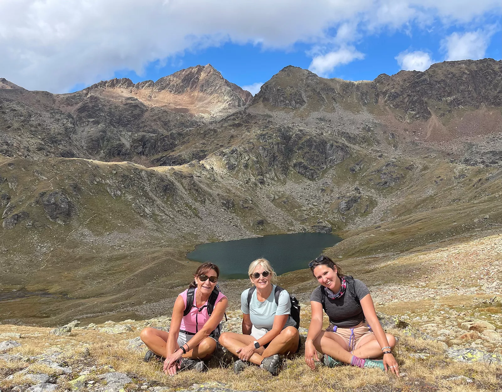 Three women sitting on a hill, with a small lake in the distance