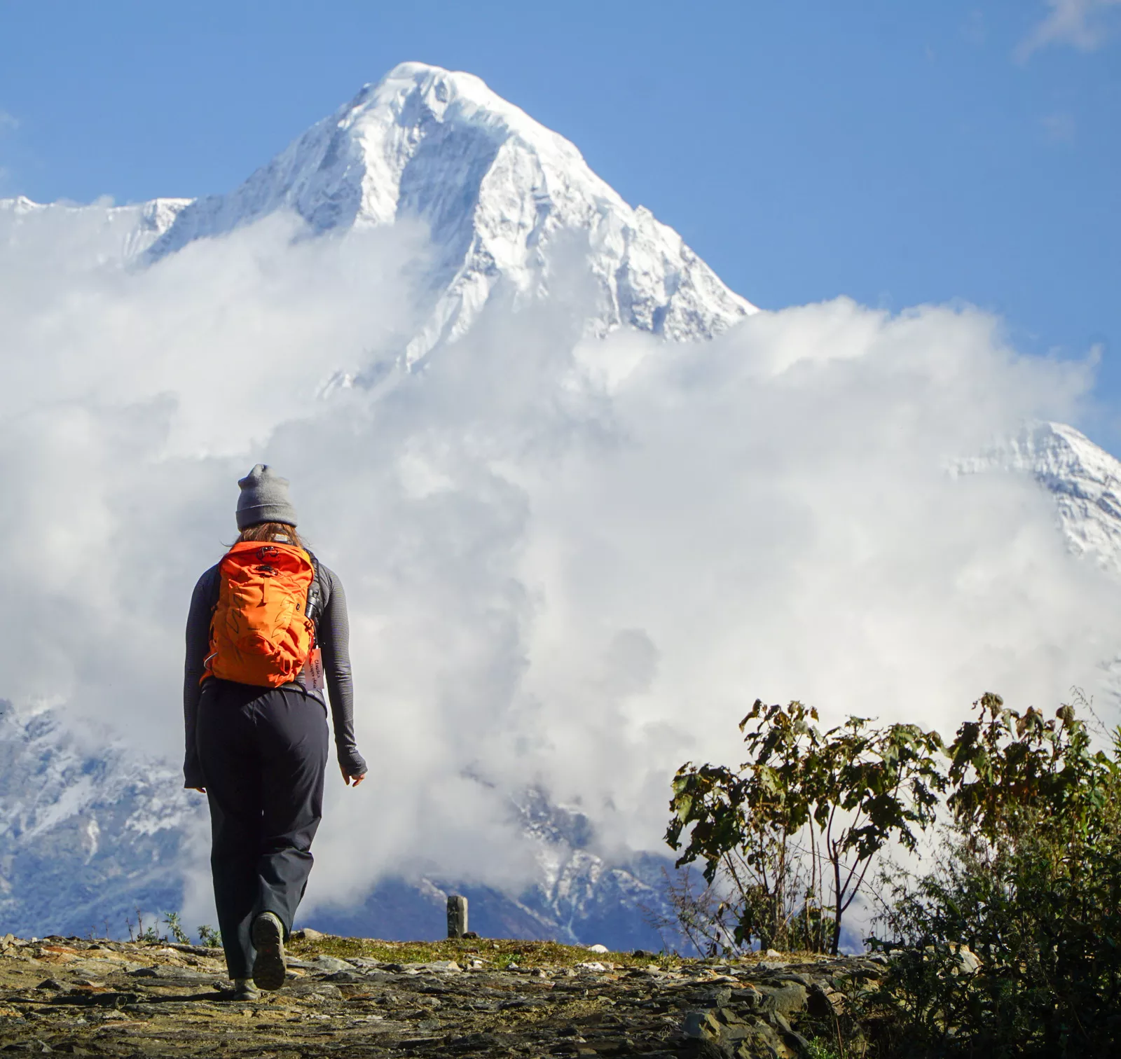 Woman with orange backpack ascending hill towards foggy mountain