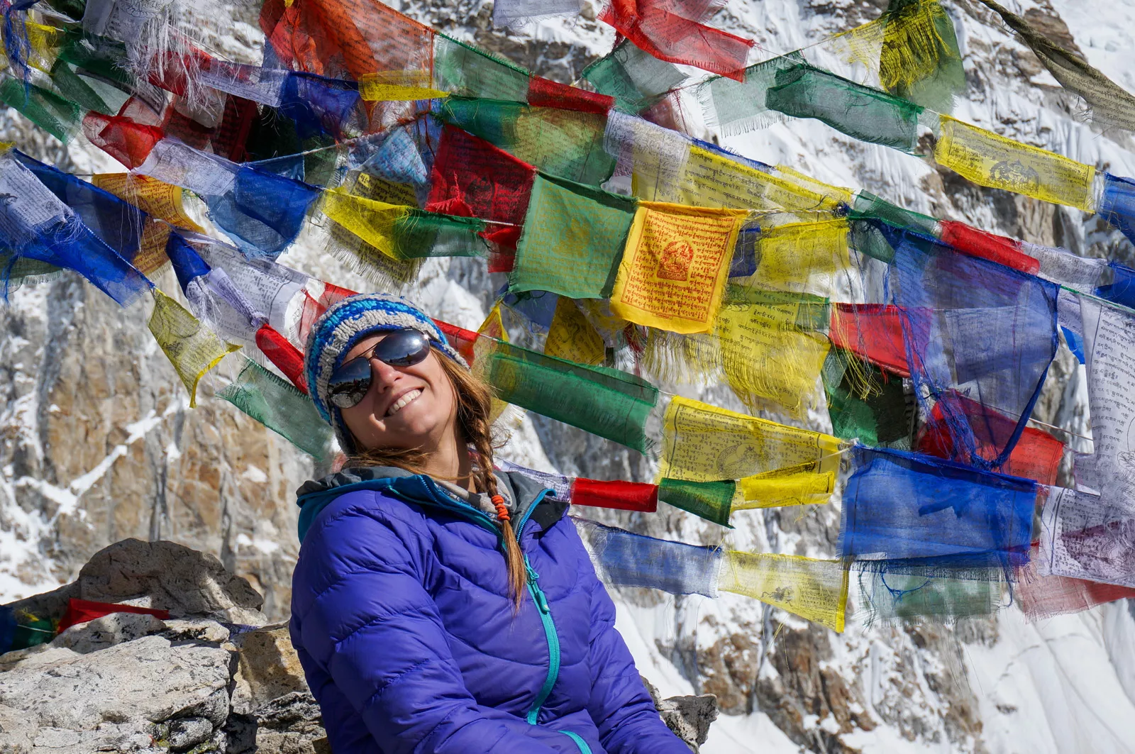 Woman smiling in front of colorful flags overlooking snowy mountains