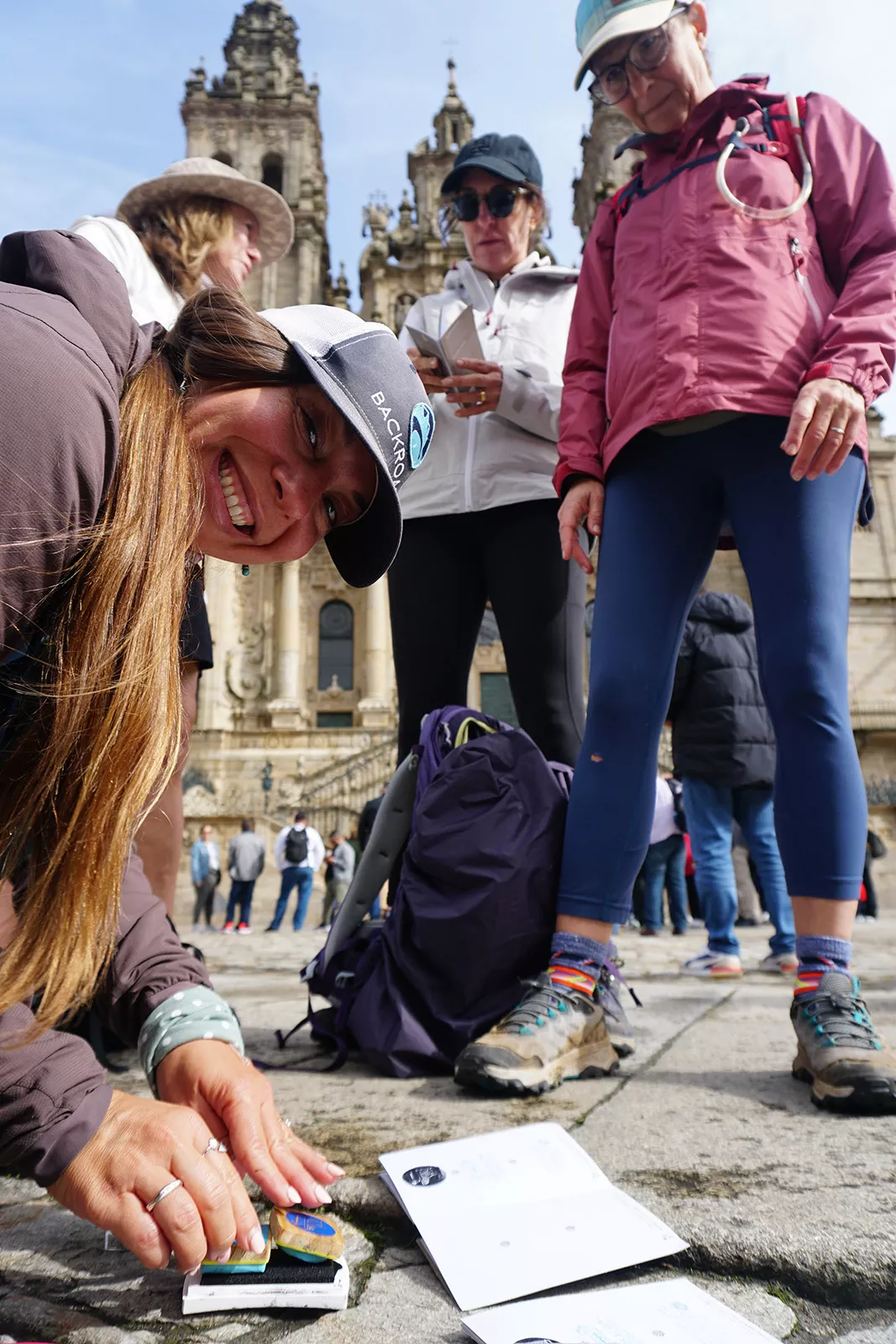 Group of people in a rustic, Spanish town center, huddled over a book with stamps