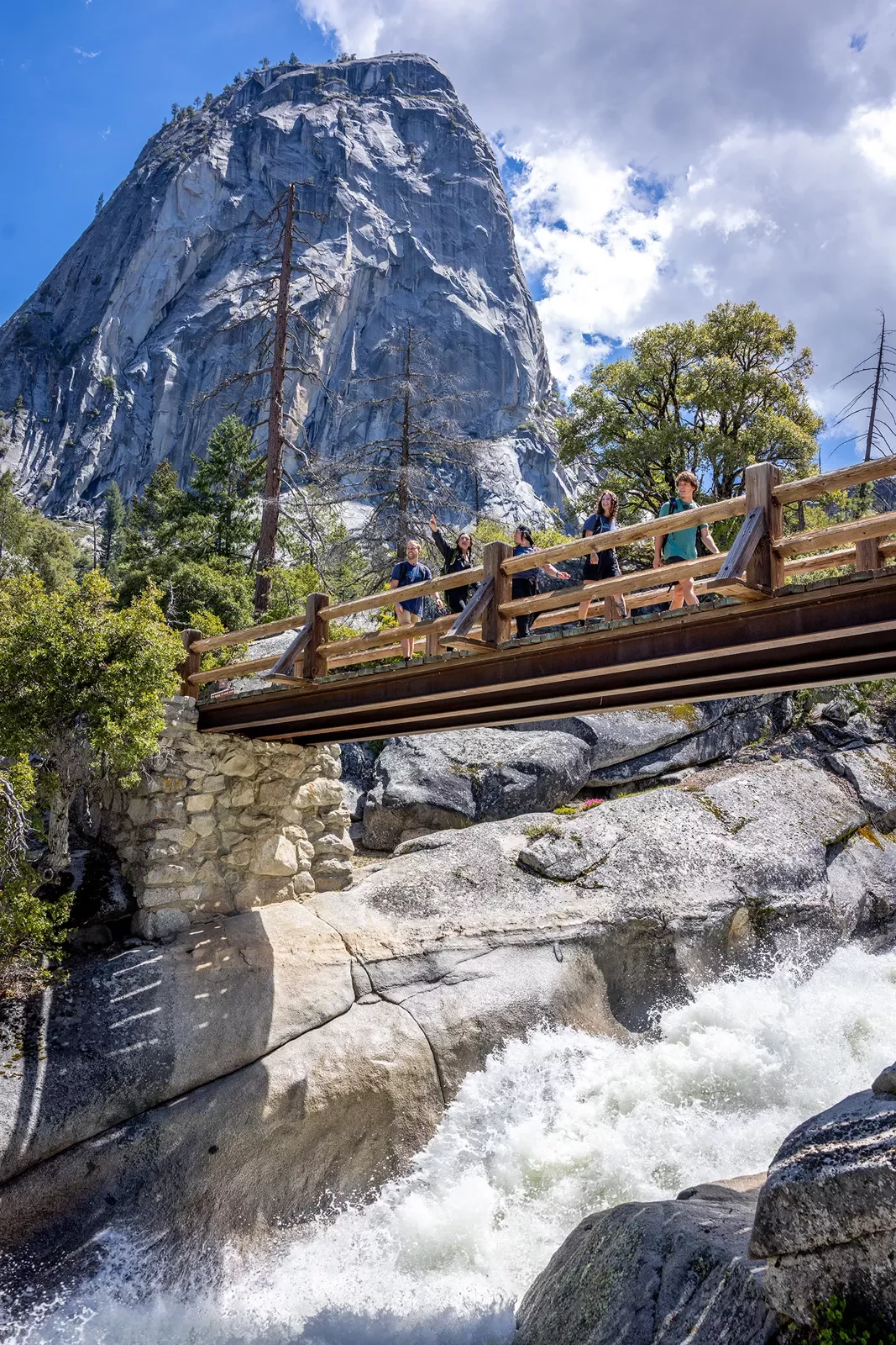 hikers cross a bridge over a roaring waterfall