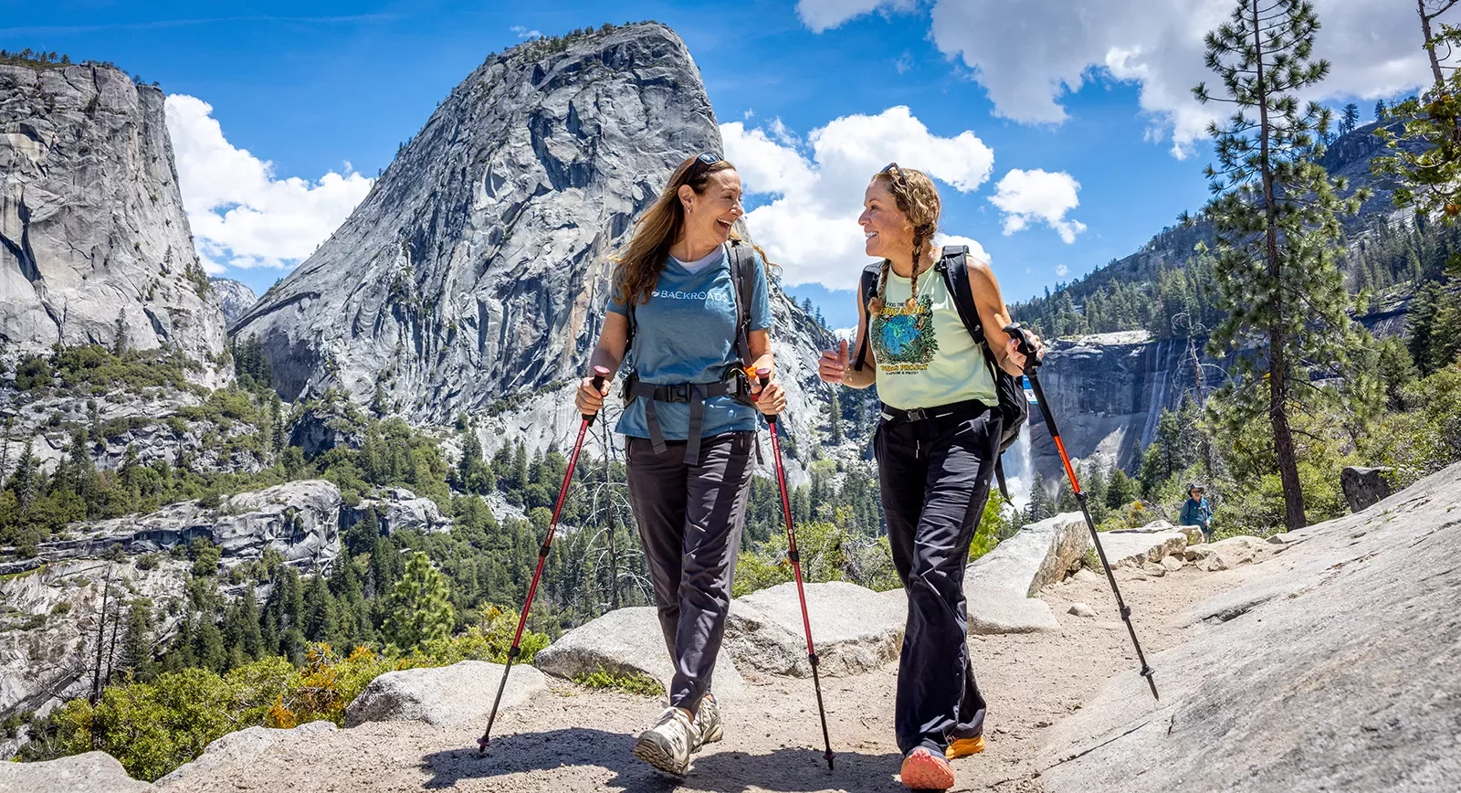 two women with hiking poles hike in yosemite