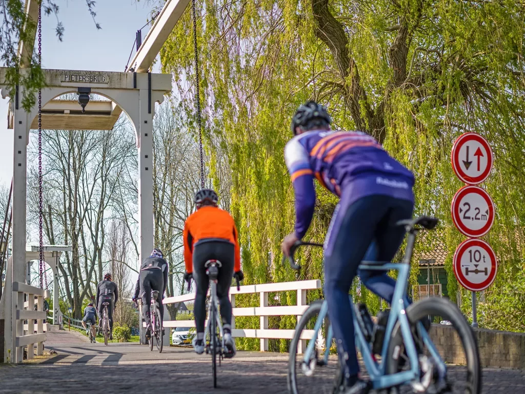 Five cyclists biking across a wooden bridge.