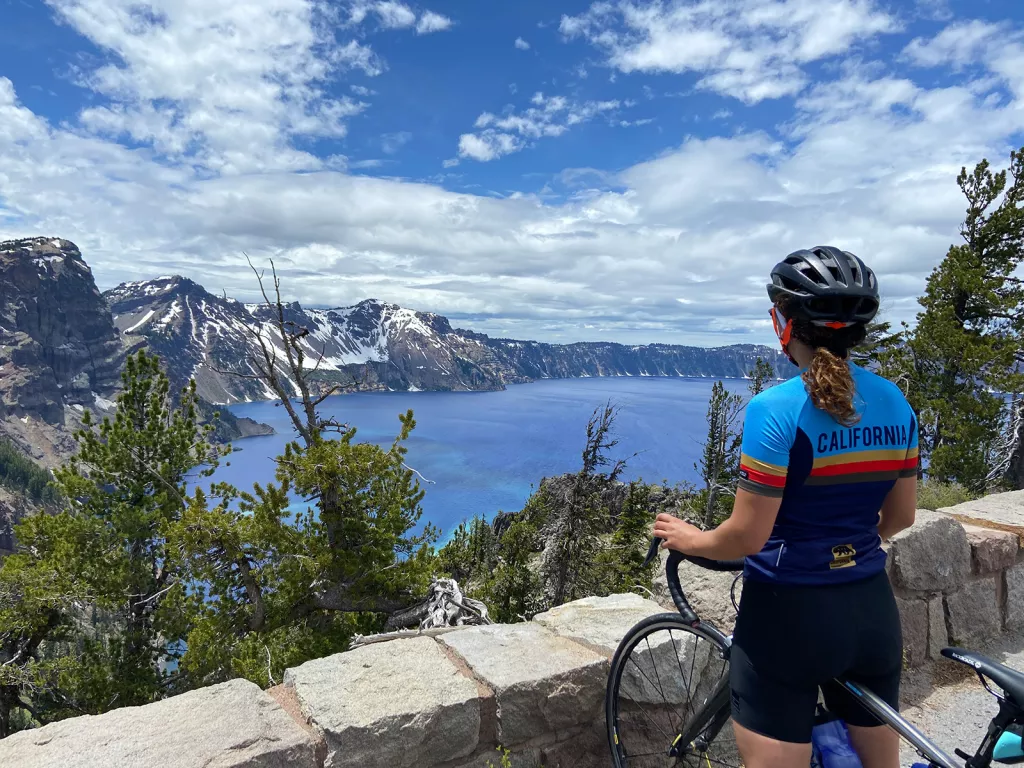 Woman standing with her bike looking out towards a lake and mountains