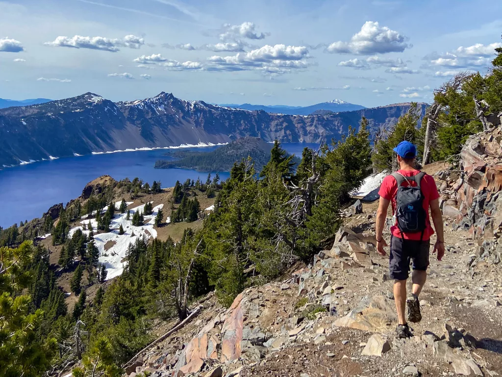 Man hiking of a stone and gravel patch looking down at a lack and valley of trees