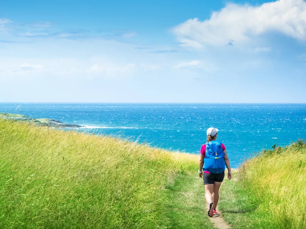 Woman hiking in a grassy field, with the ocean in the distance