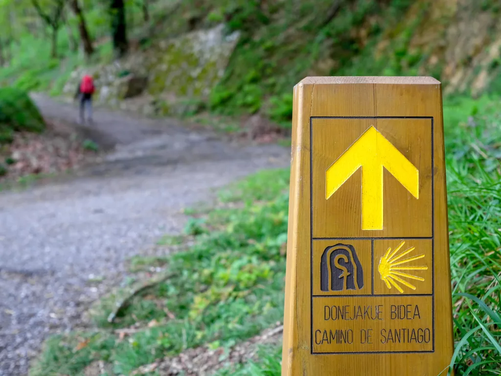 Hiking sign on a trail, with a person walking on a gravel path