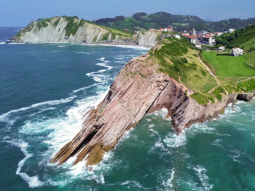 Slanted cliff on the coast of an ocean, with a small town in the distance