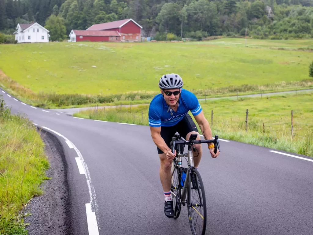 Man riding bike on asphalt road through a grassy field