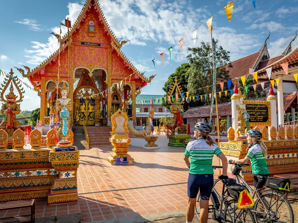 Two women walking their bikes as they approach a shrine