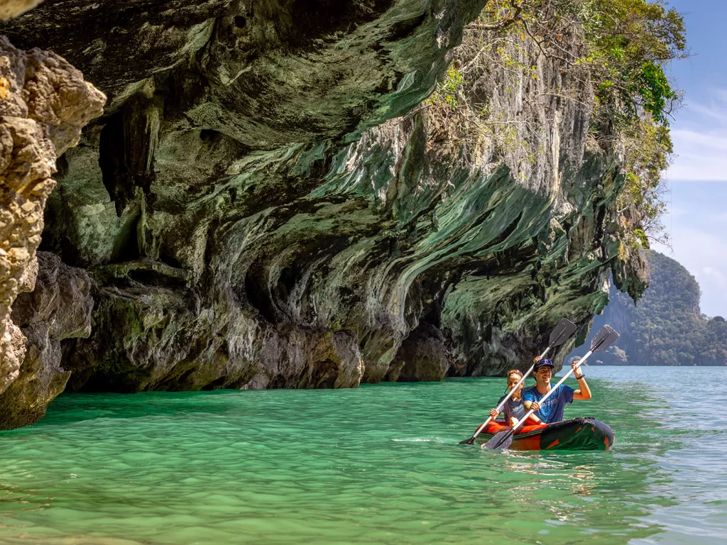 Man and woman paddling in a red kayak in the ocean, under a cliff