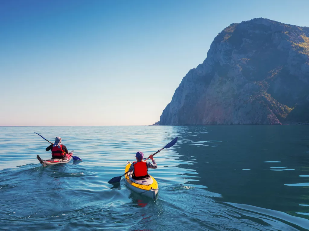 Two people paddling on kayaks in the middle of the ocean