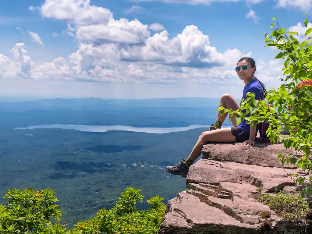 Woman sitting on a cliff with large trees on ground floor