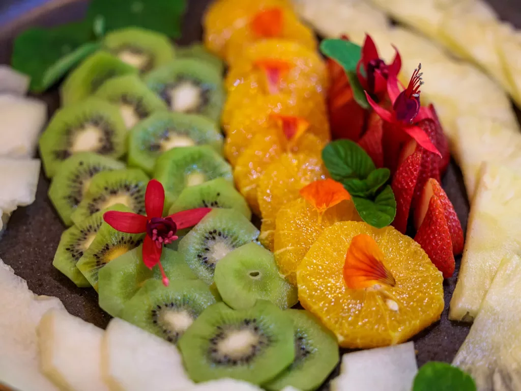 Plate full of sliced fruits, including kiwi, orange, strawberries and pineapple