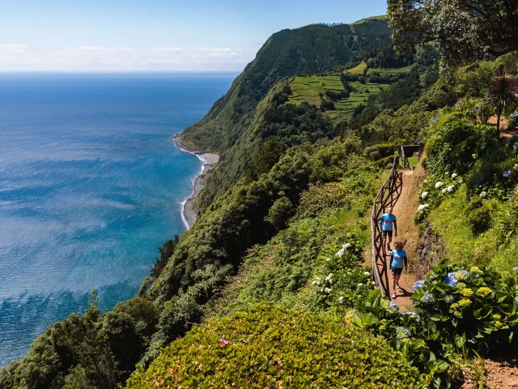 Two people walking on a dirt path along a cliff looking out to the ocean