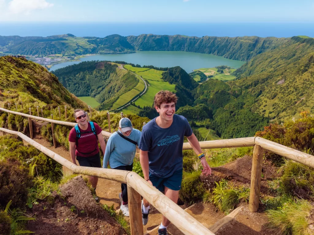 Three people walking on a dirt path that is on top of a hill, with a large valley in the background