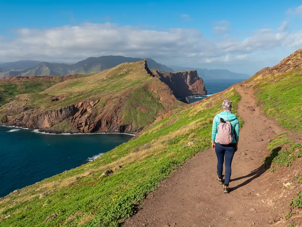 Woman walking on a dirt path on a hill, with a lake on the ground level