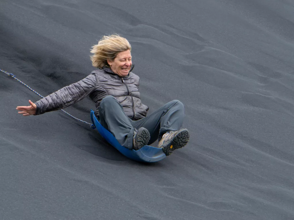 Woman sitting on a plastic barrel seat, going down a sandy hill