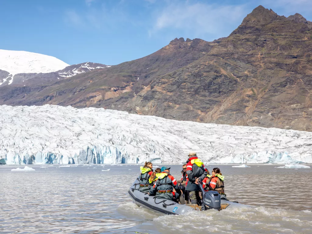 Group of people on a gray raft, going towards snow caps