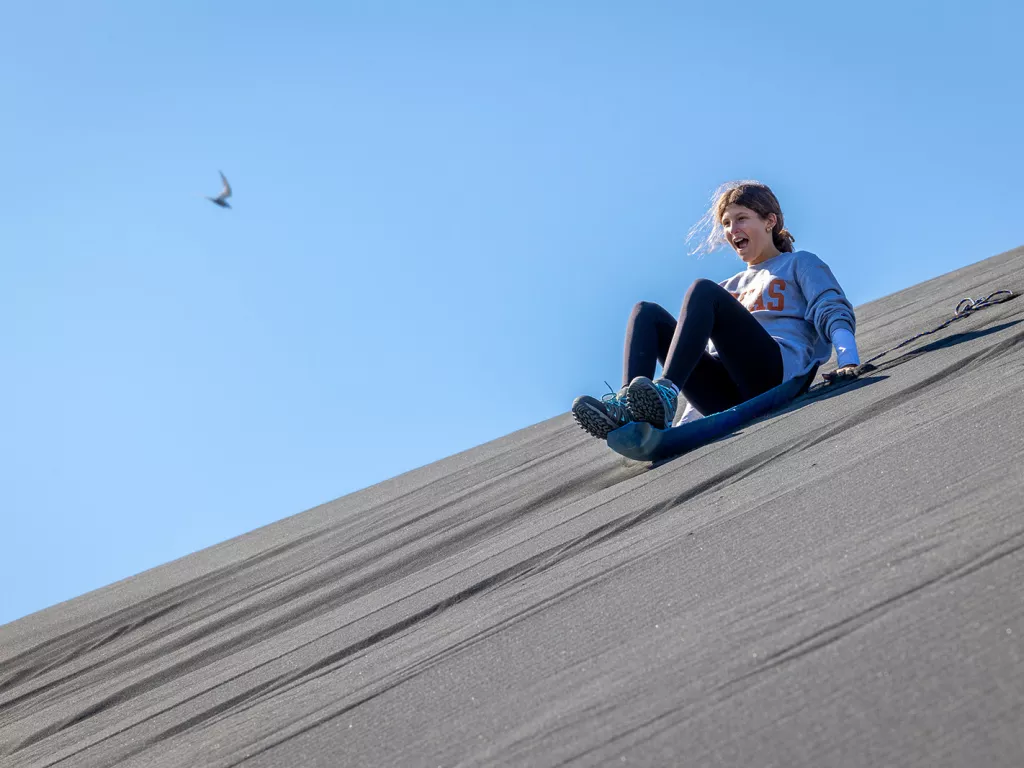 Girl on a plastic sled sliding down a hill of sand