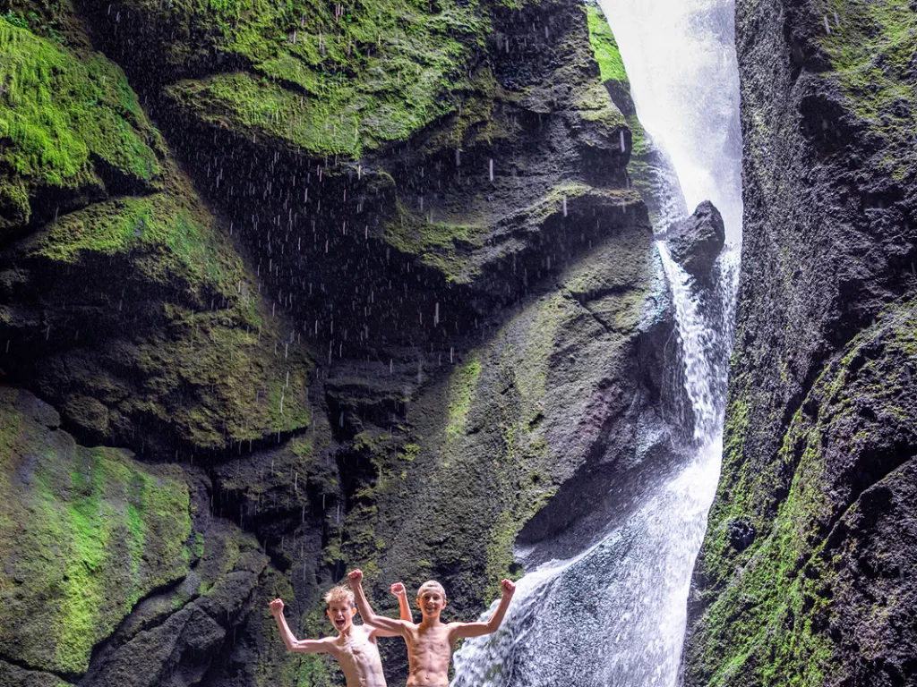 Two boys standing on a rock next to a waterfall