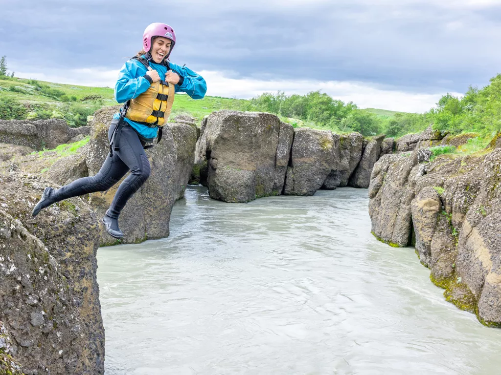 Woman wearing a helmet and life vest jumping into a small lake