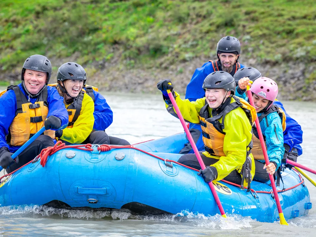 Group of men and women on a blue raft, paddling and smiling