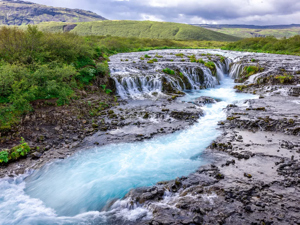 Small waterfall with an active river in the middle of a grass field