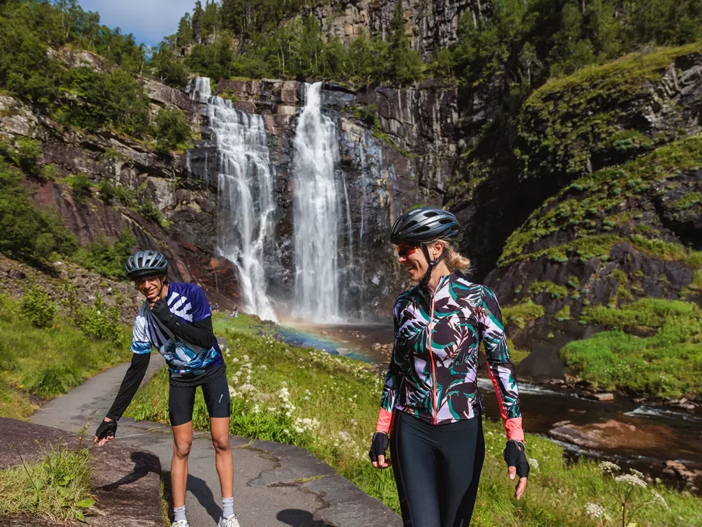 Two guests in cycling kits with a waterfall