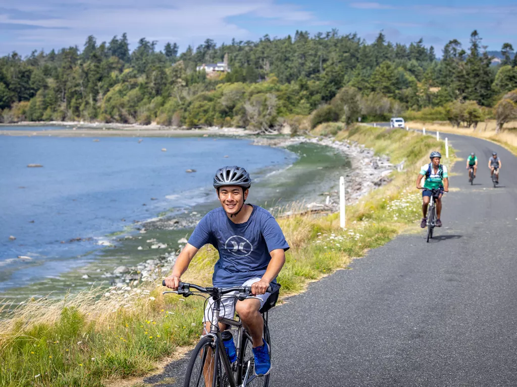 Man riding a bike on an asphalt road with a lake behind him