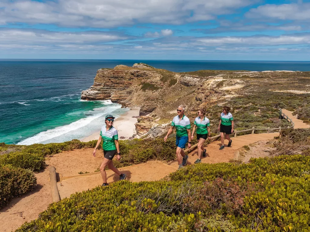 Four people hike up a sandy beach front road