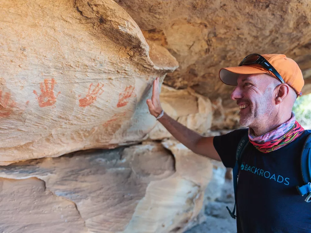 A man holds his hand up to handprints on a stone wall