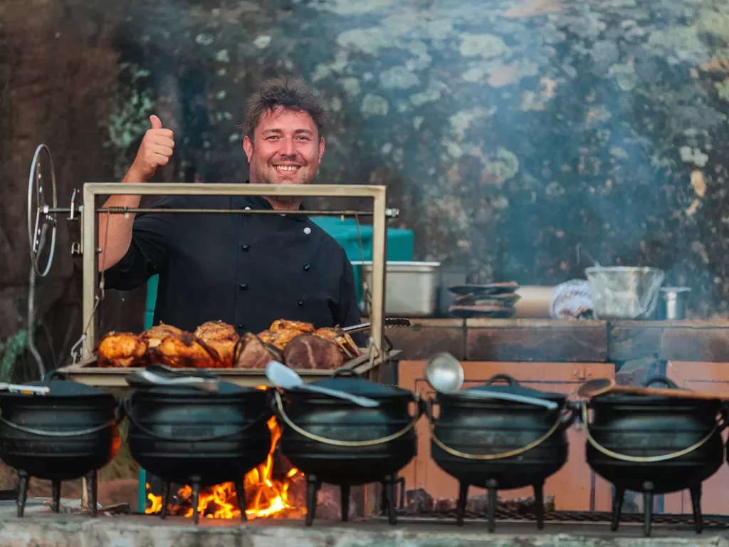 A man stands behind cauldrons of cooking food