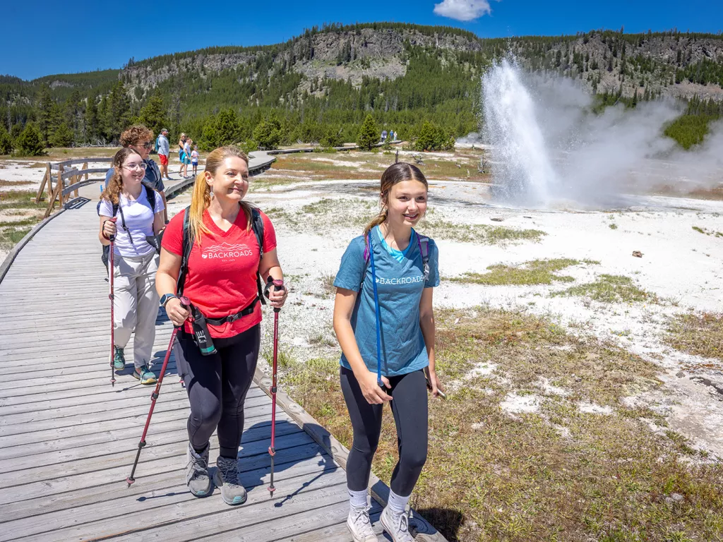 One woman and two girls hiking next to an active geyser