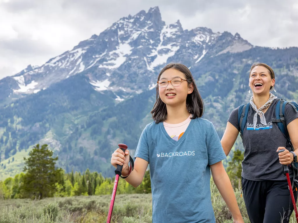 Woman and girl with walking poles hiking in a grassy valley