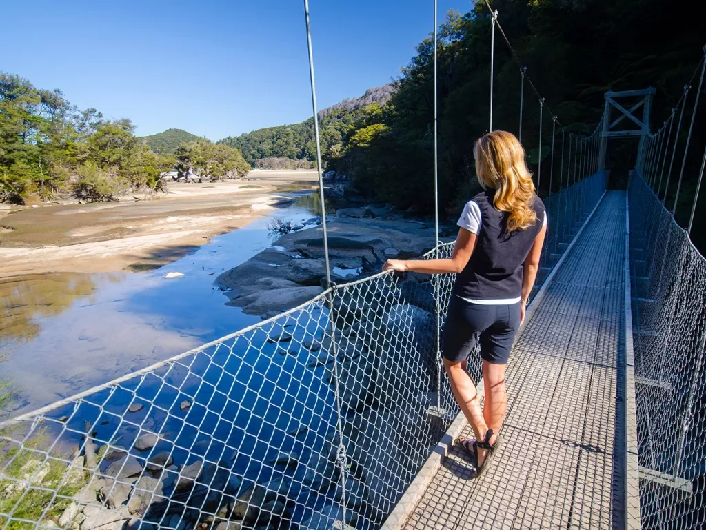 Woman on a metal bridge looking down at a small pond