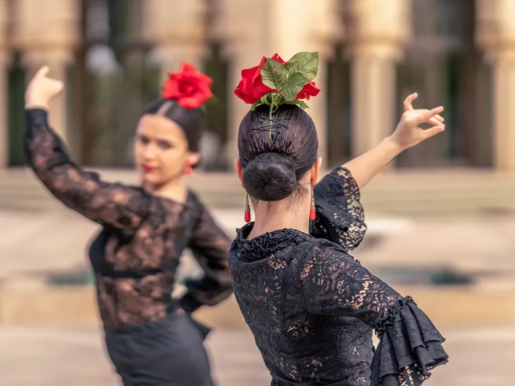 Two women dancing with large red roses on their heads