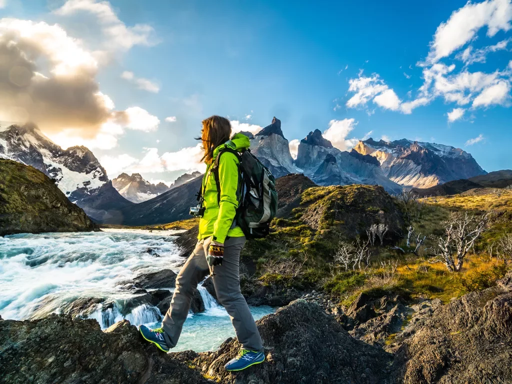 Person in green jacket crossing through rocks with a river in the background