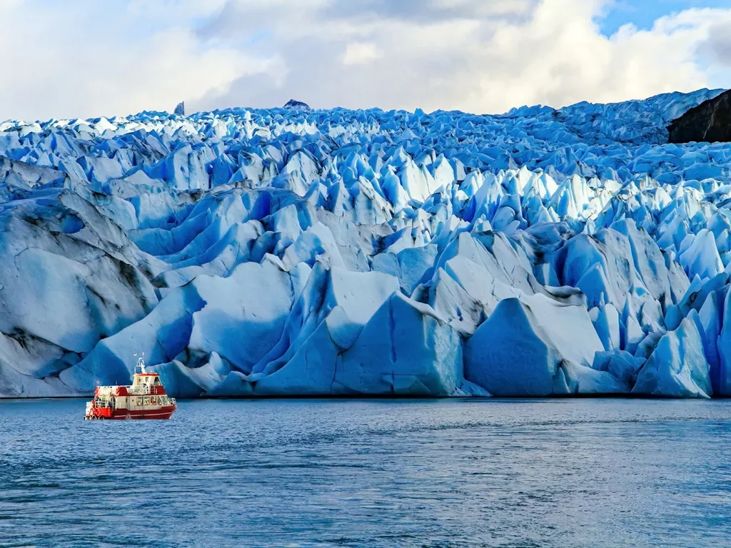 Jagged snow caps with a red and white boat traveling in front