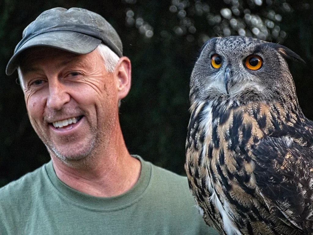 Man wearing a hat smiling next to an owl