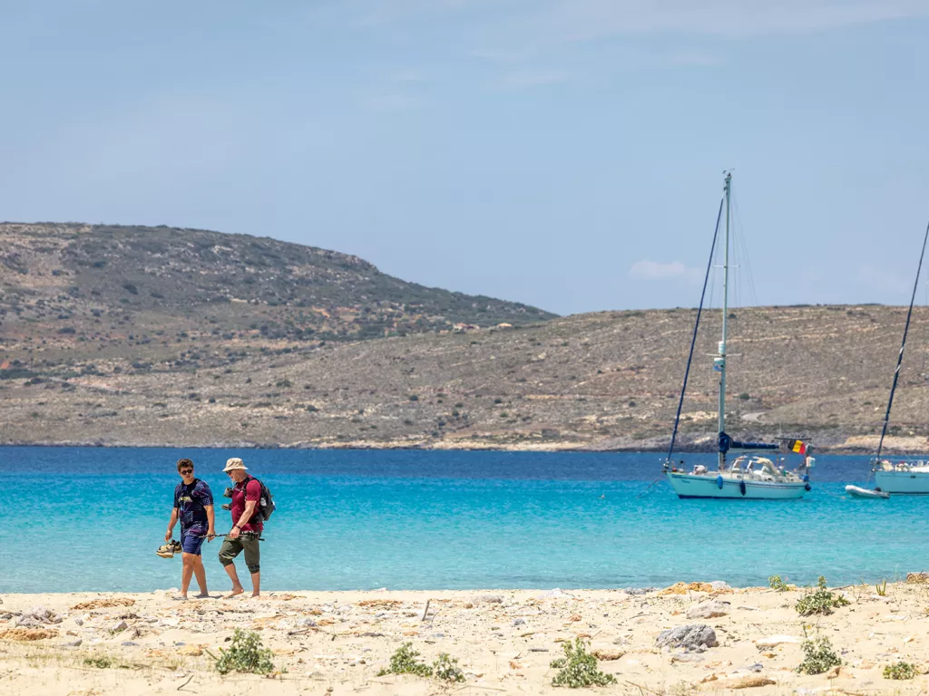 Two people on the beach walking next to the ocean with their shoes in hand