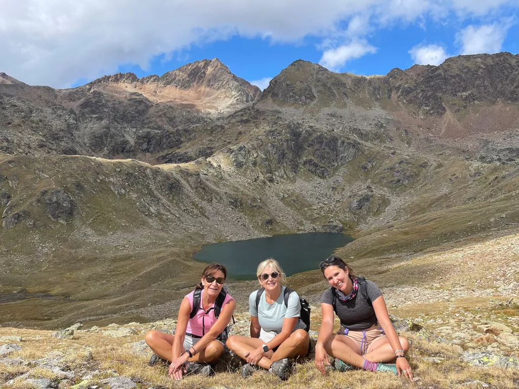 Three women sitting on a hill, with a small lake in the distance