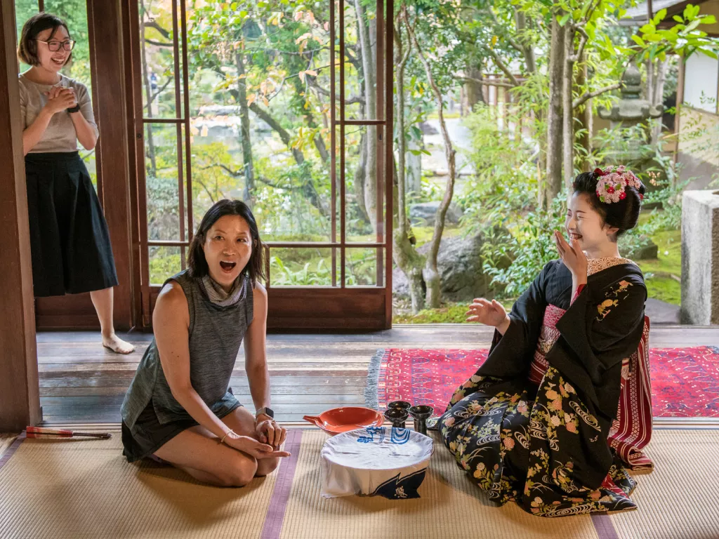 Woman sitting in front of a geisha, kneeling on the ground