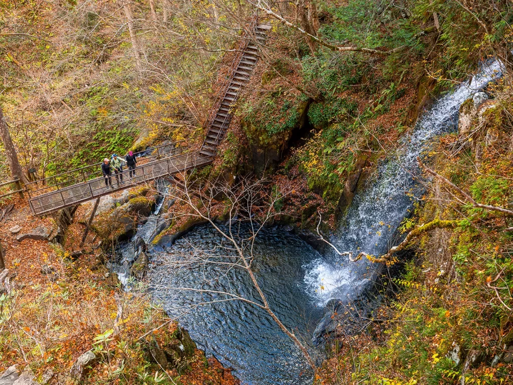 a waterfall falling into a lake, next to a hiking path