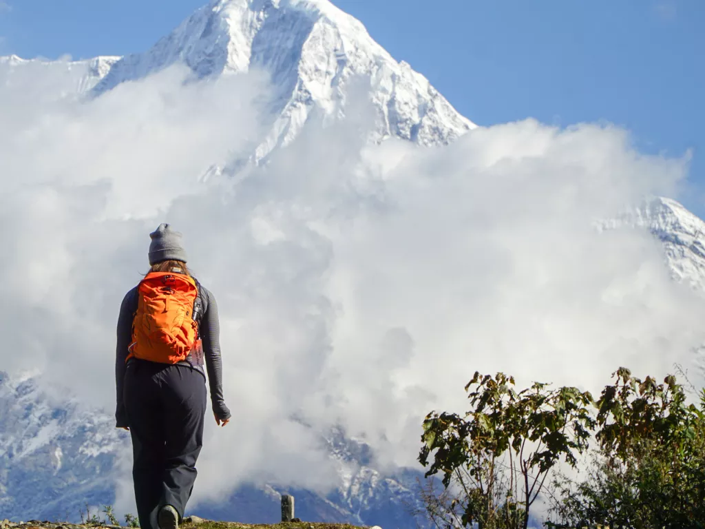 Woman with orange backpack ascending hill towards foggy mountain