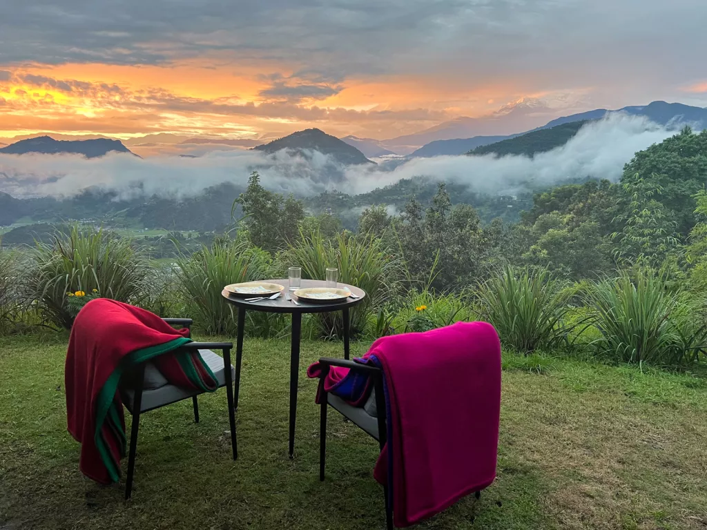 A table and chair with blankets over them overlooking foggy mountains