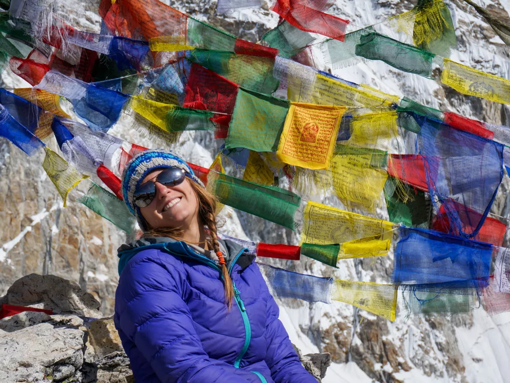 Woman smiling in front of colorful flags overlooking snowy mountains